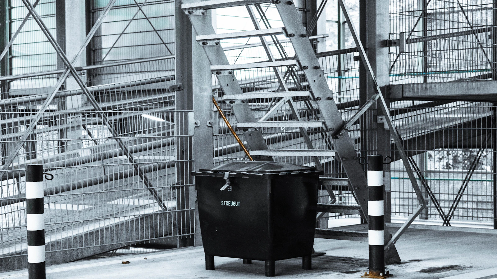black trash bin near gray metal fence