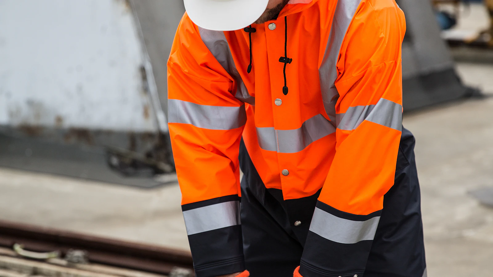 a man in an orange safety jacket working on a metal rail