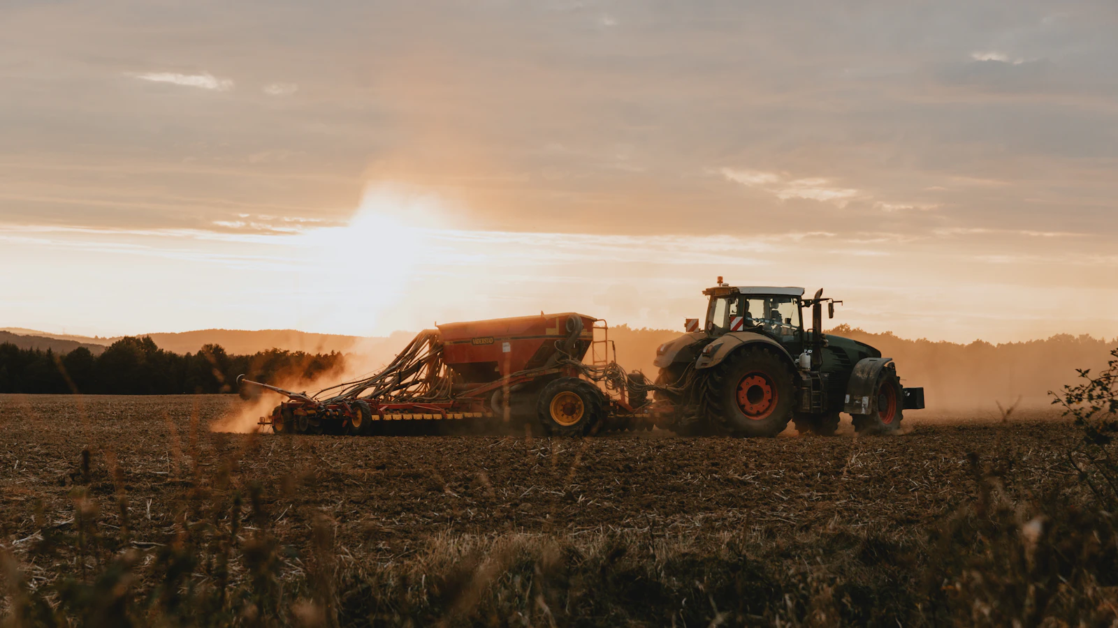 a tractor is driving through a field at sunset