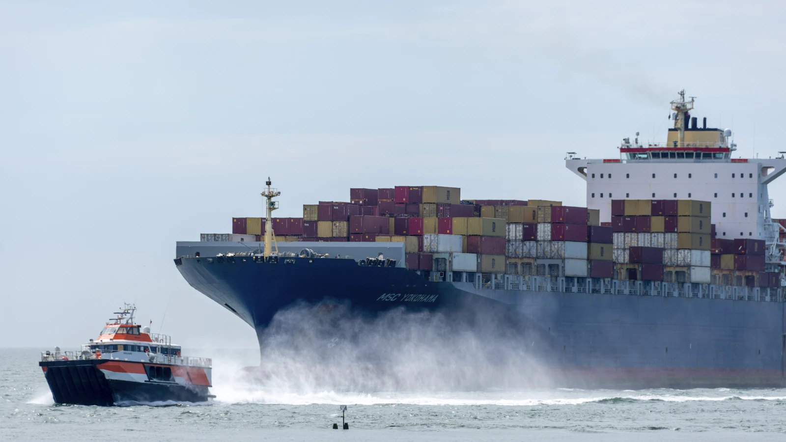 a large cargo ship in the ocean with a tug boat nearby