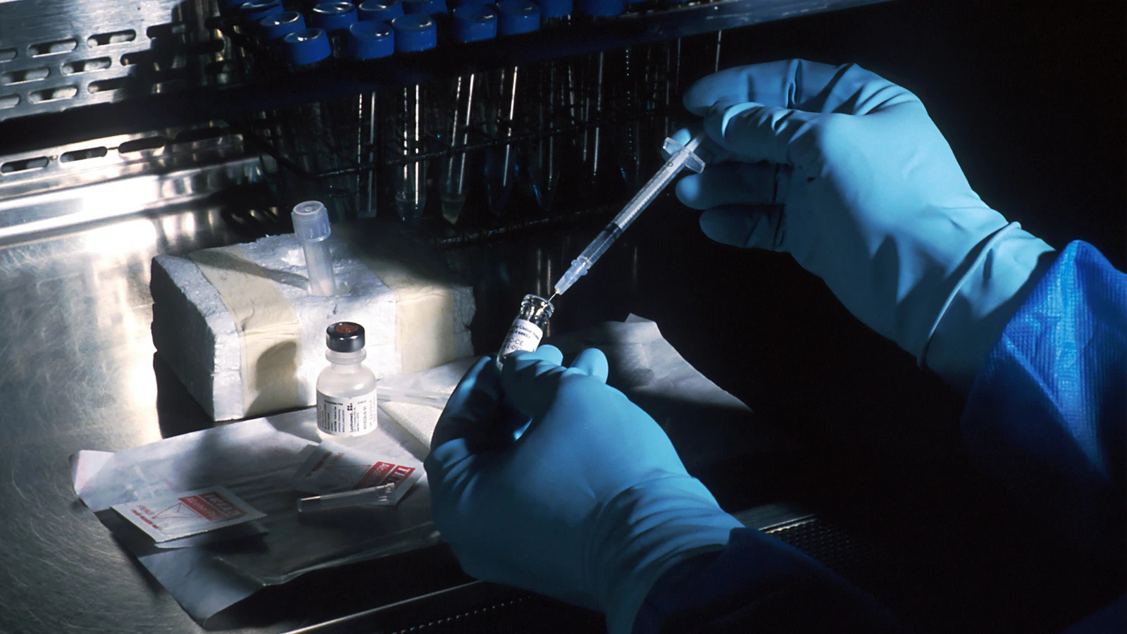 gloved hands drawing vaccine from vial with syringe